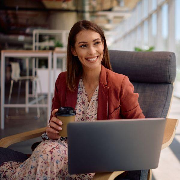 A woman holds a coffee cup while using a laptop in a modern office
