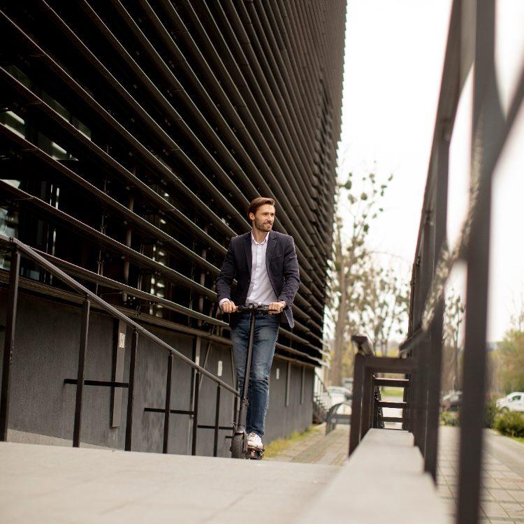 Man riding an electric scooter beside a slatted office facade