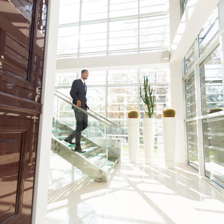 Man in a suit walking down a glass staircase in a bright lobby