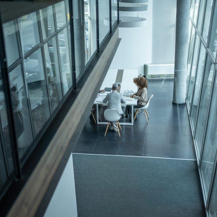 Overhead view of three colleagues meeting at a table in a glass-walled atrium