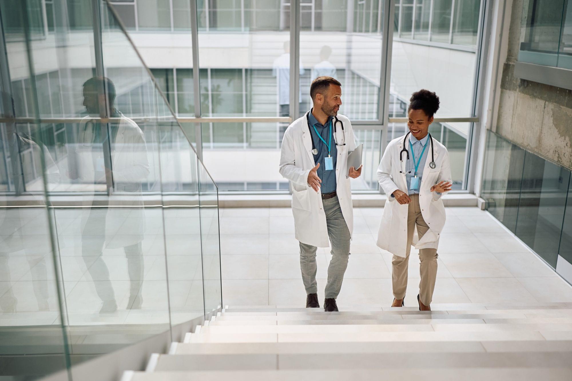 Two doctors in white coats talking as they climb a bright hospital staircase