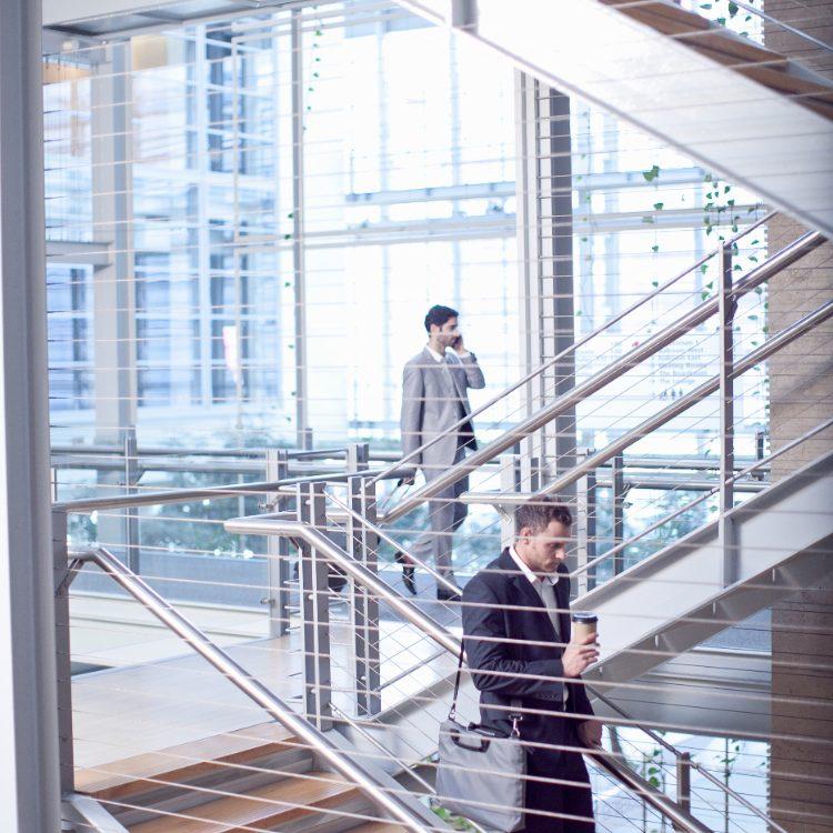 Two men in suits on the open stairs of a glass office atrium