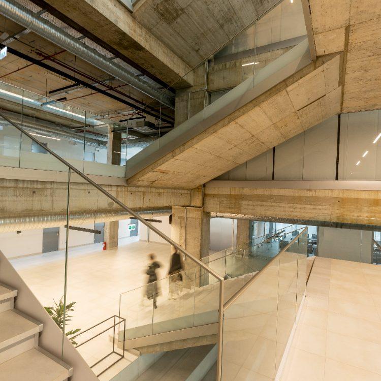 Two people walking through a concrete and glass office atrium