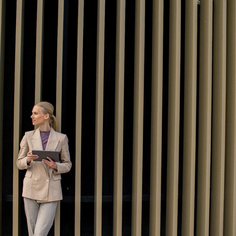 Woman holding a tablet in front of a slatted architectural wall