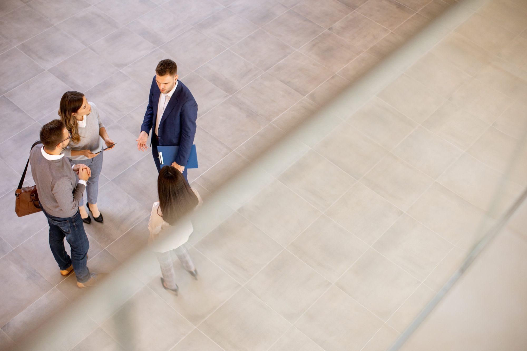 Four colleagues in conversation on a tiled floor, seen from above through a glass balustrade